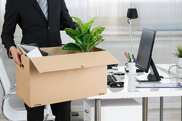 Midsection of businessman carrying cardboard box by desk in office moving