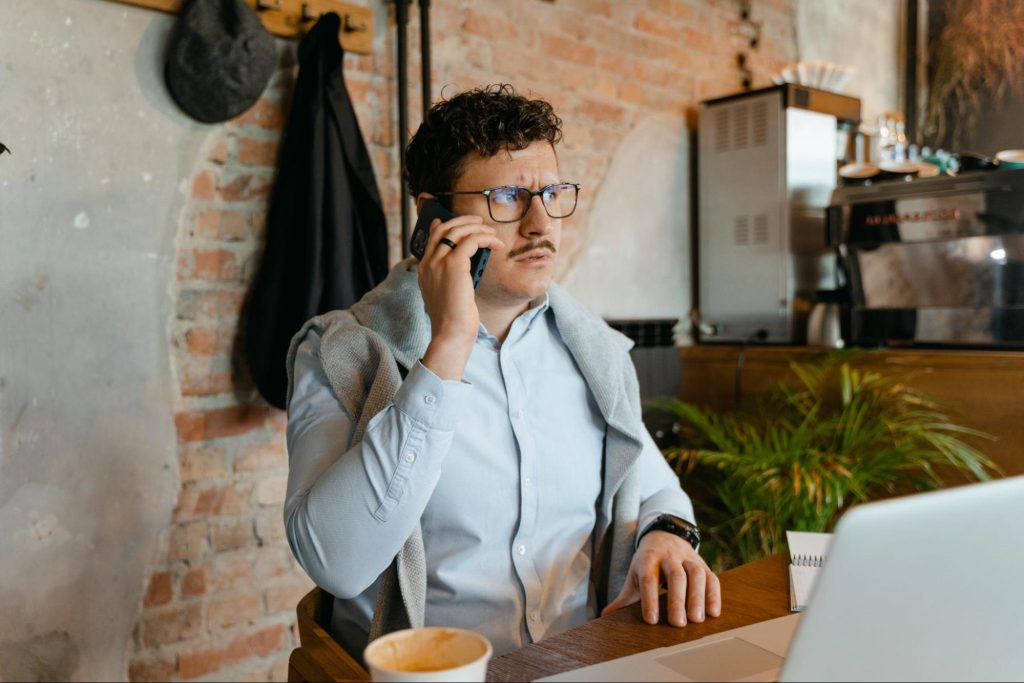 Confused man sitting at computer talking on phone